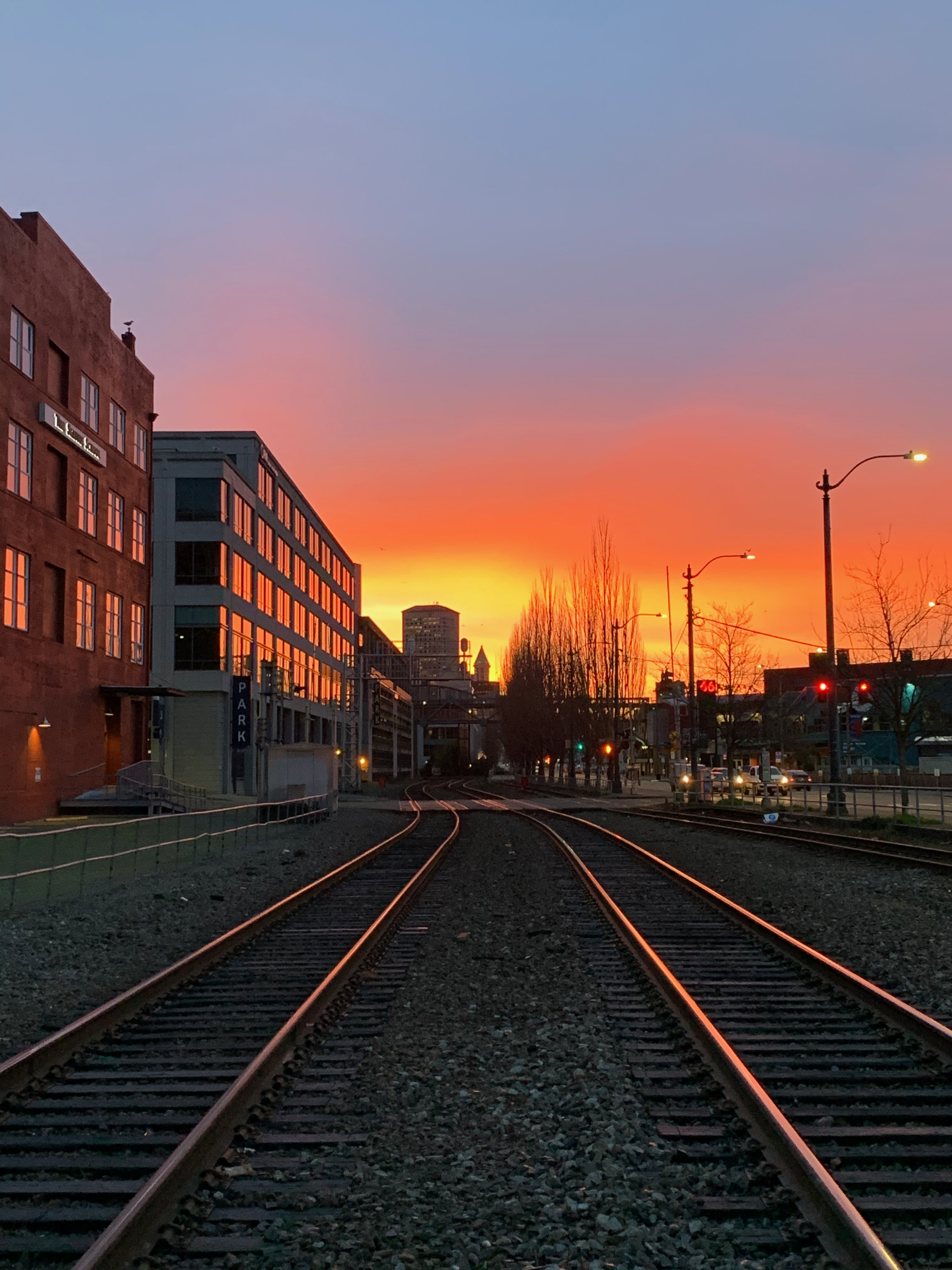 Railroad tracks leading toward a fiery orange sunrise over downtown Seattle